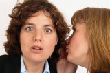 Two women whisper a secret in close up of ear and mouth.